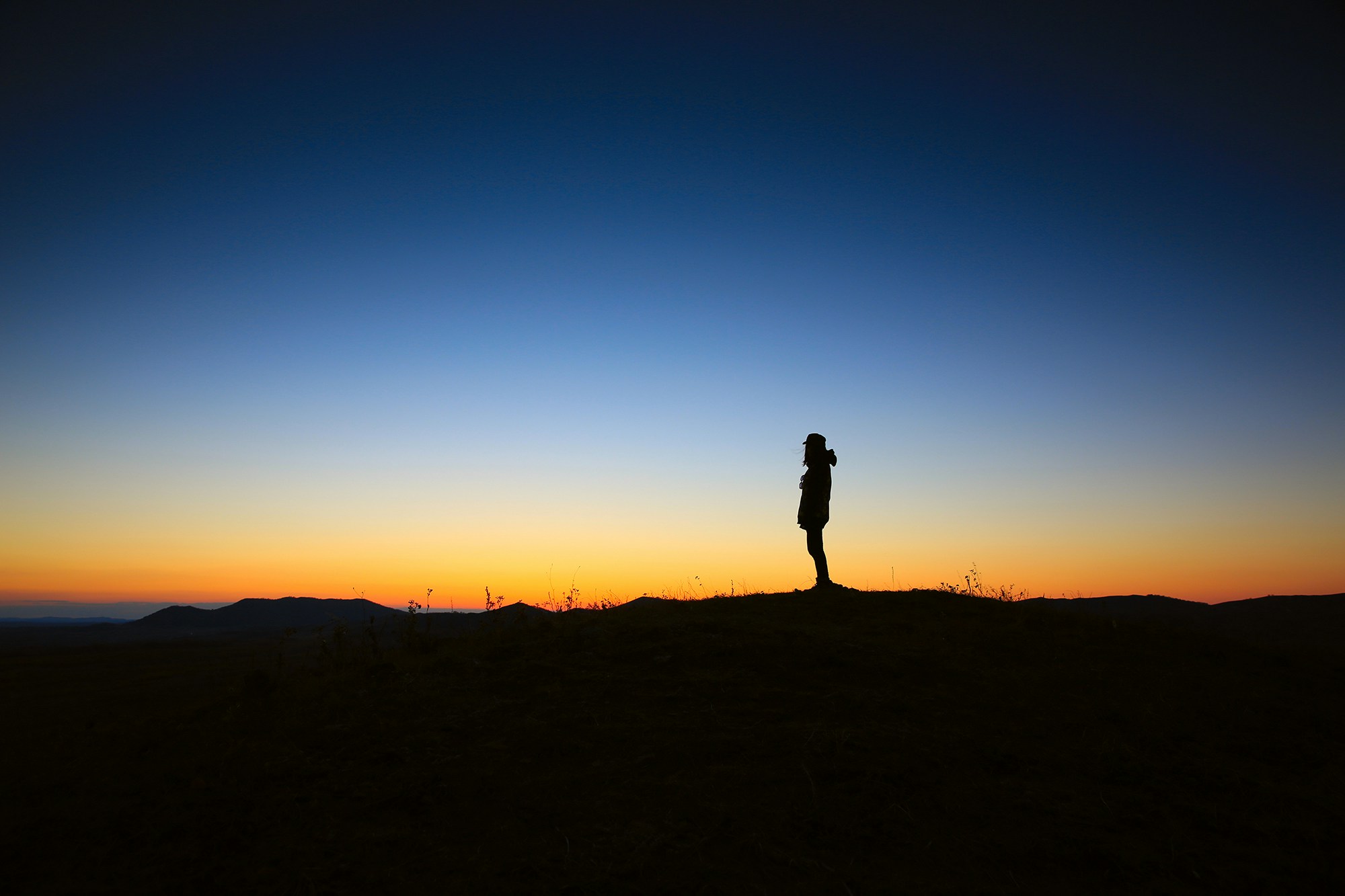 Silhouette of a man retreating to the outdoors at dawn, standing against a stunning mountain skyline with the sunrise casting vibrant colors across the sky, symbolizing stillness, freedom, and perspective in nature caring for the soul.